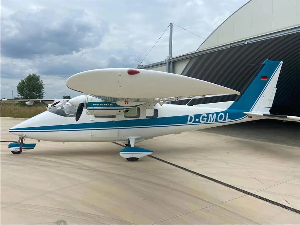 A white and blue Partenavia P.68 aircraft with registration D-GMOL parked on an airfield next to a hangar.
