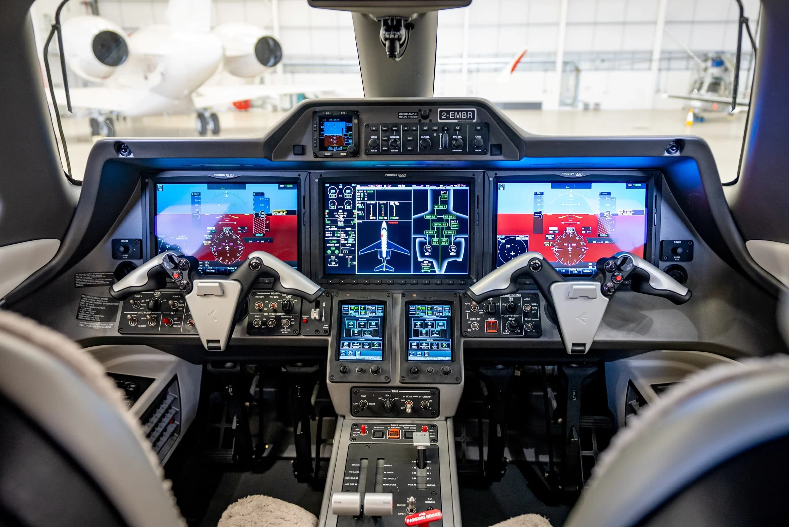 The modern cockpit of an Embraer Phenom 300E, featuring multiple large digital displays and control yokes.