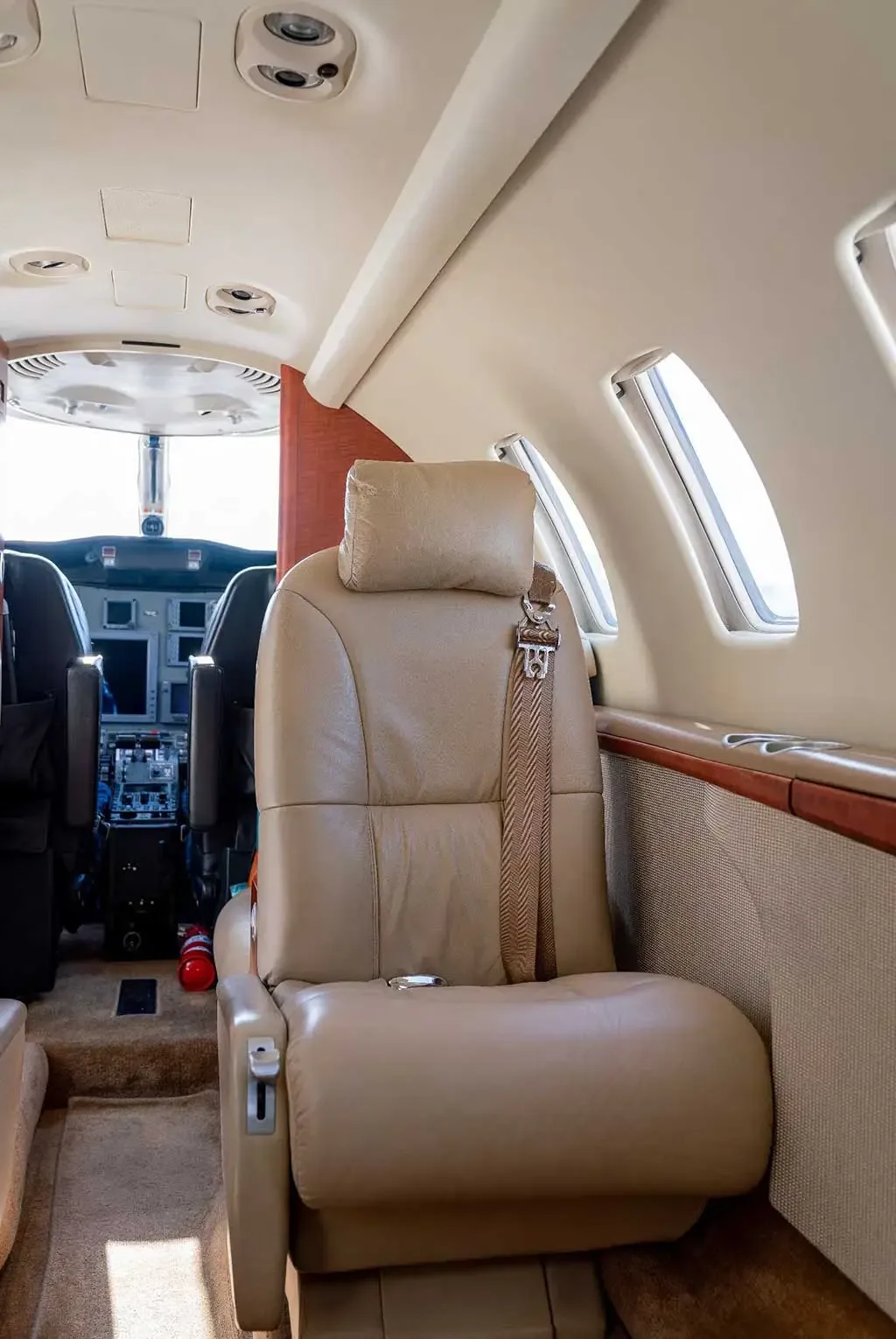 A close-up of a beige leather passenger seat inside the private jet's cabin, with the cockpit visible ahead.