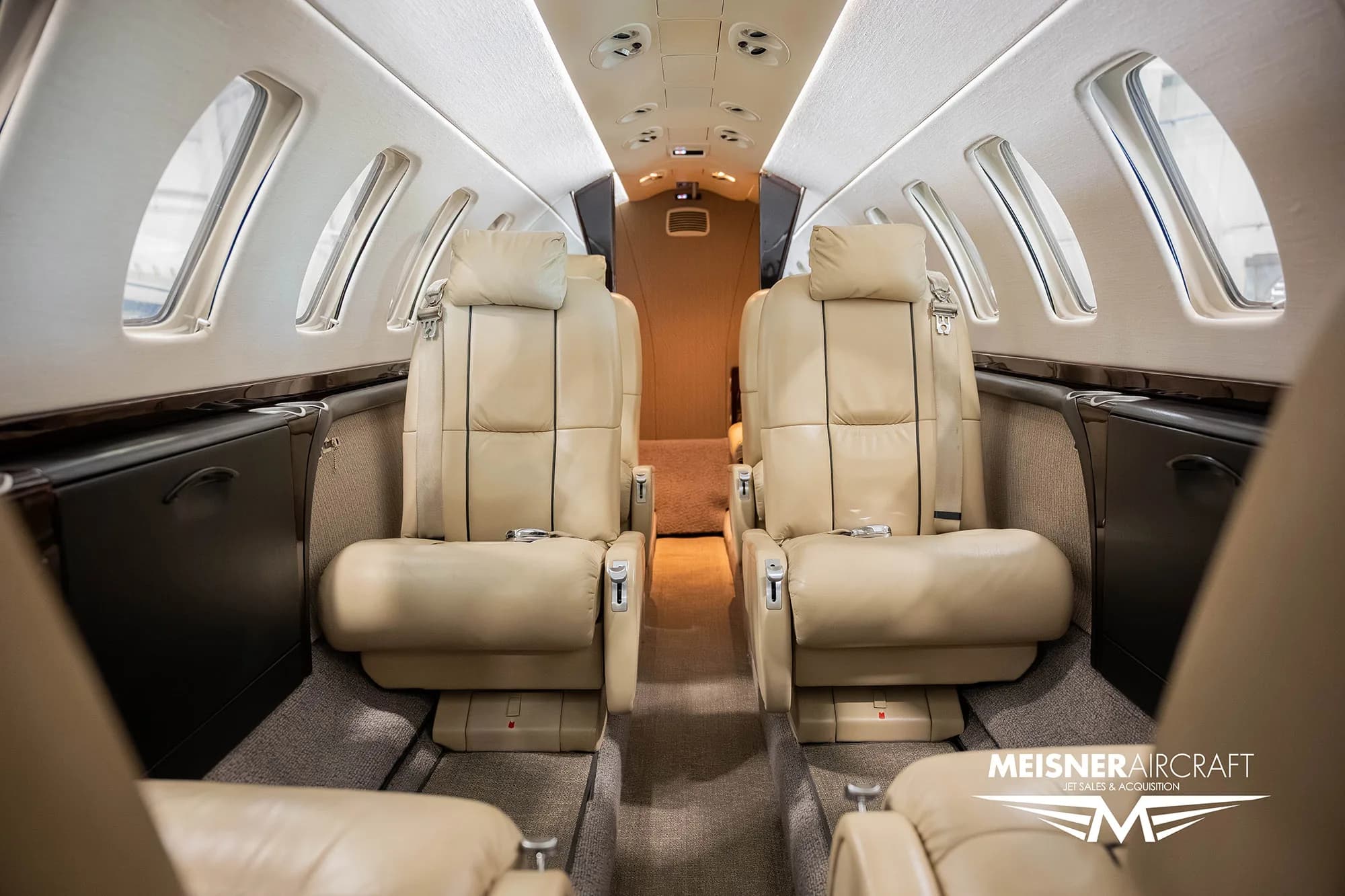 The interior cabin of a business jet, featuring two rows of beige leather seats, viewed from the rear.