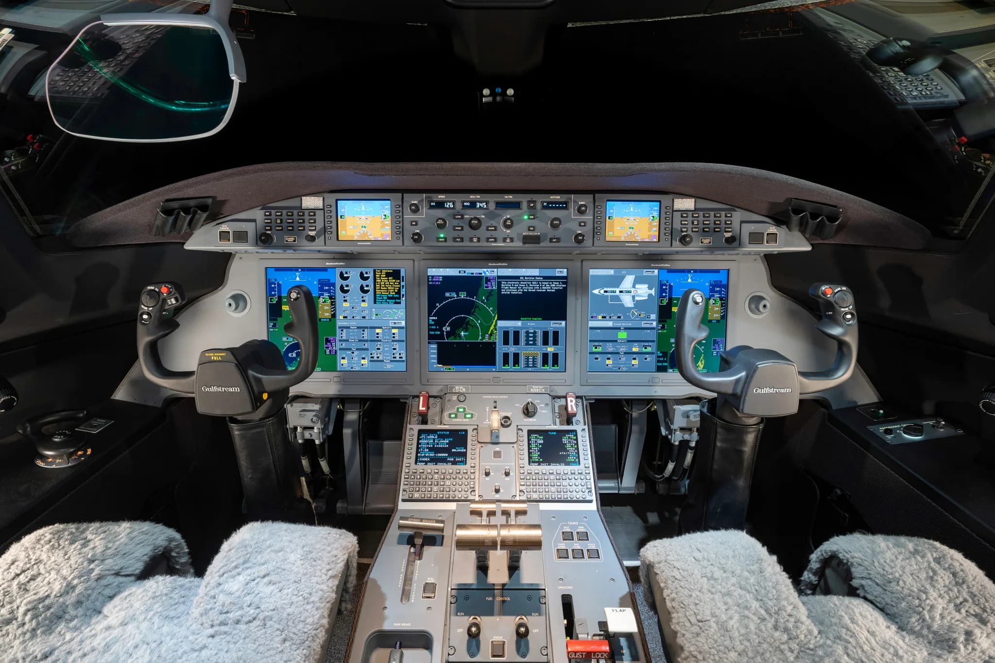 The cockpit of a modern business jet, featuring multiple digital displays, control yokes, and a central control panel.