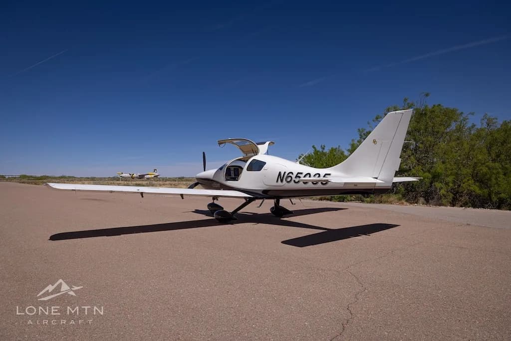 A white and black single-engine aircraft, N65035, with its gull-wing doors open, seen from the rear on an airport tarmac.