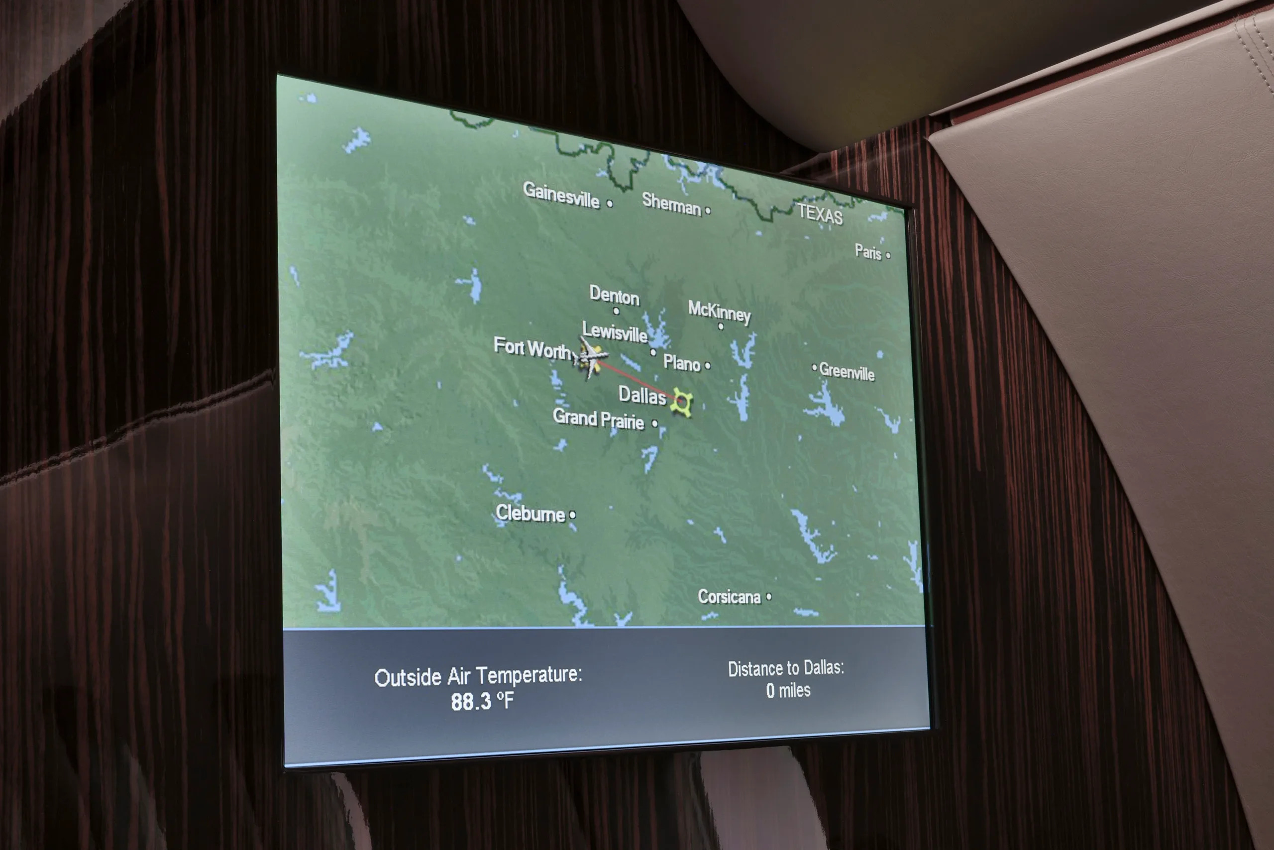 An in-flight entertainment screen displaying a map of Texas with cities like Dallas and Fort Worth, and current temperature.