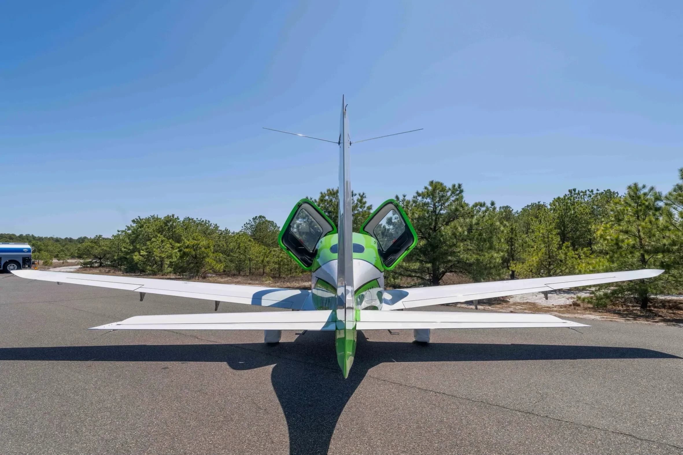 A rear view of the green and white Cirrus SR22T aircraft, N260AV, with its gull-wing doors open, parked on an airfield.