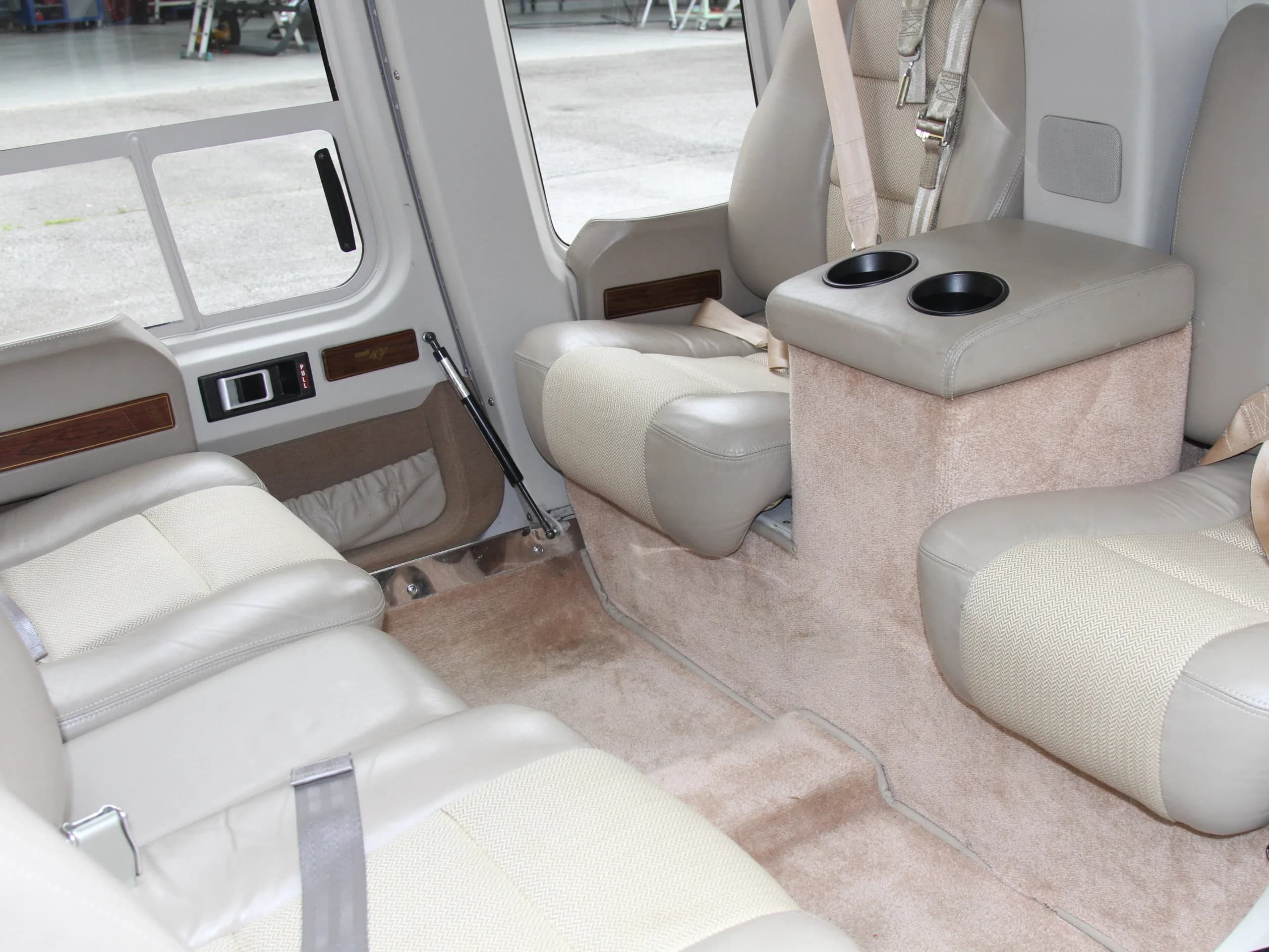 The helicopter's interior features tan leather seats, a center console with cupholders, and carpeted flooring.