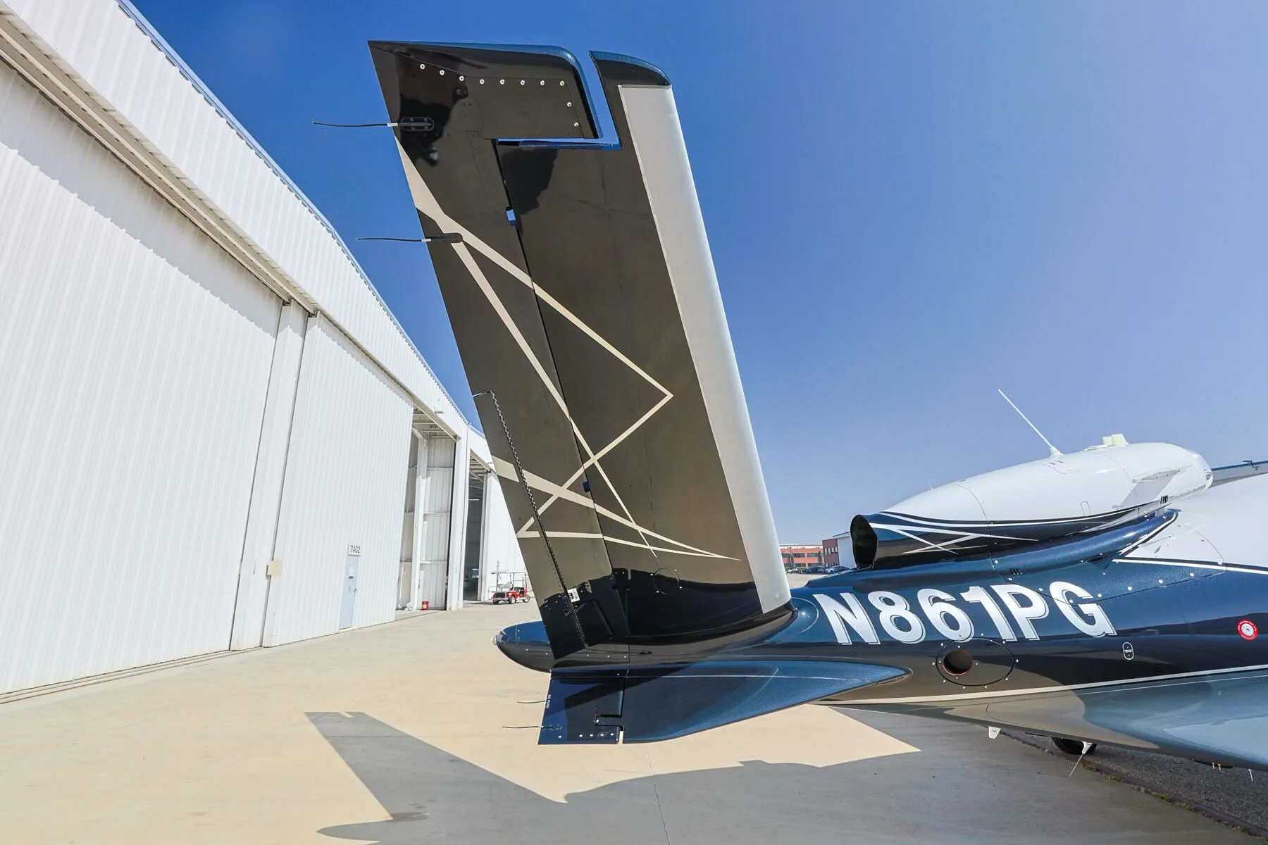 Close-up of the V-tail of a Cirrus Vision Jet (N861PG) with a geometric design, parked next to a hangar.