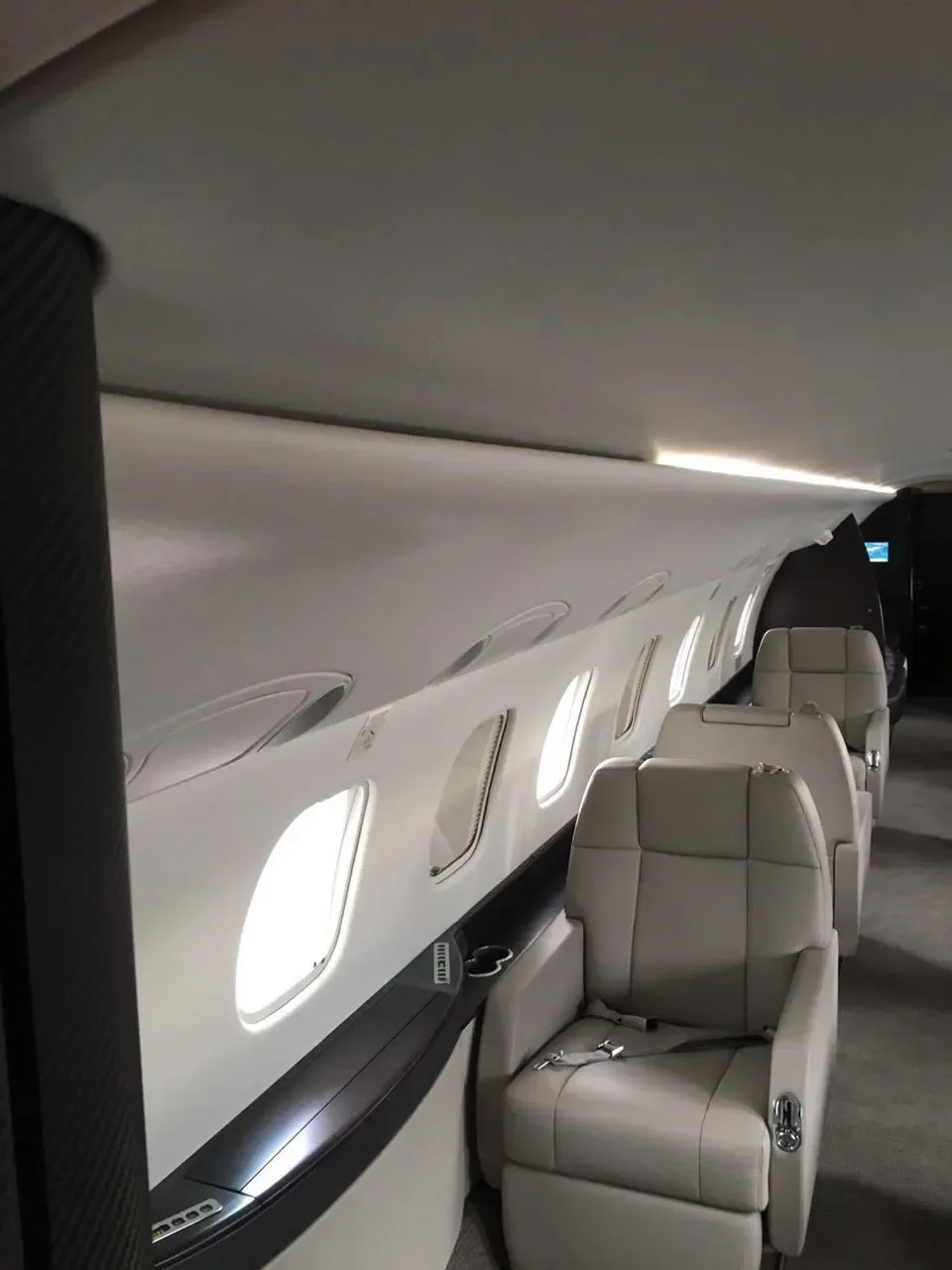 A row of light beige leather seats next to large windows in a private jet cabin.