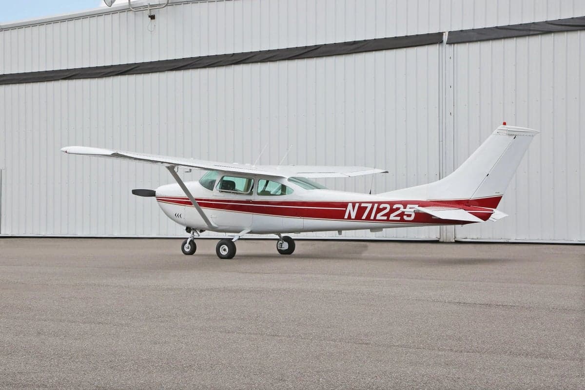 Side view of a Cessna aircraft with a white and red paint scheme parked in front of a hangar, showing the tail number N71225.