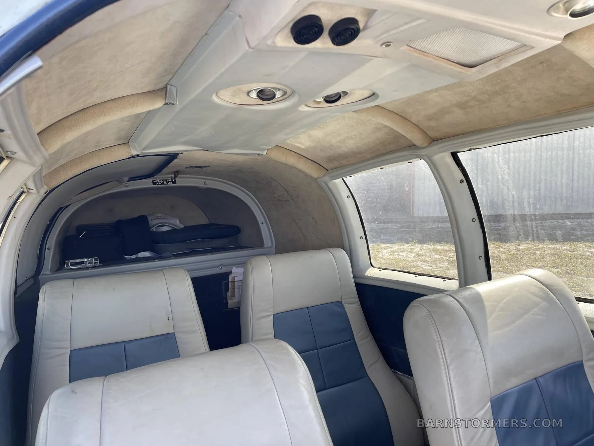 View of the aircraft's rear cabin interior, showing two rows of white and blue leather seats and an aft baggage area.