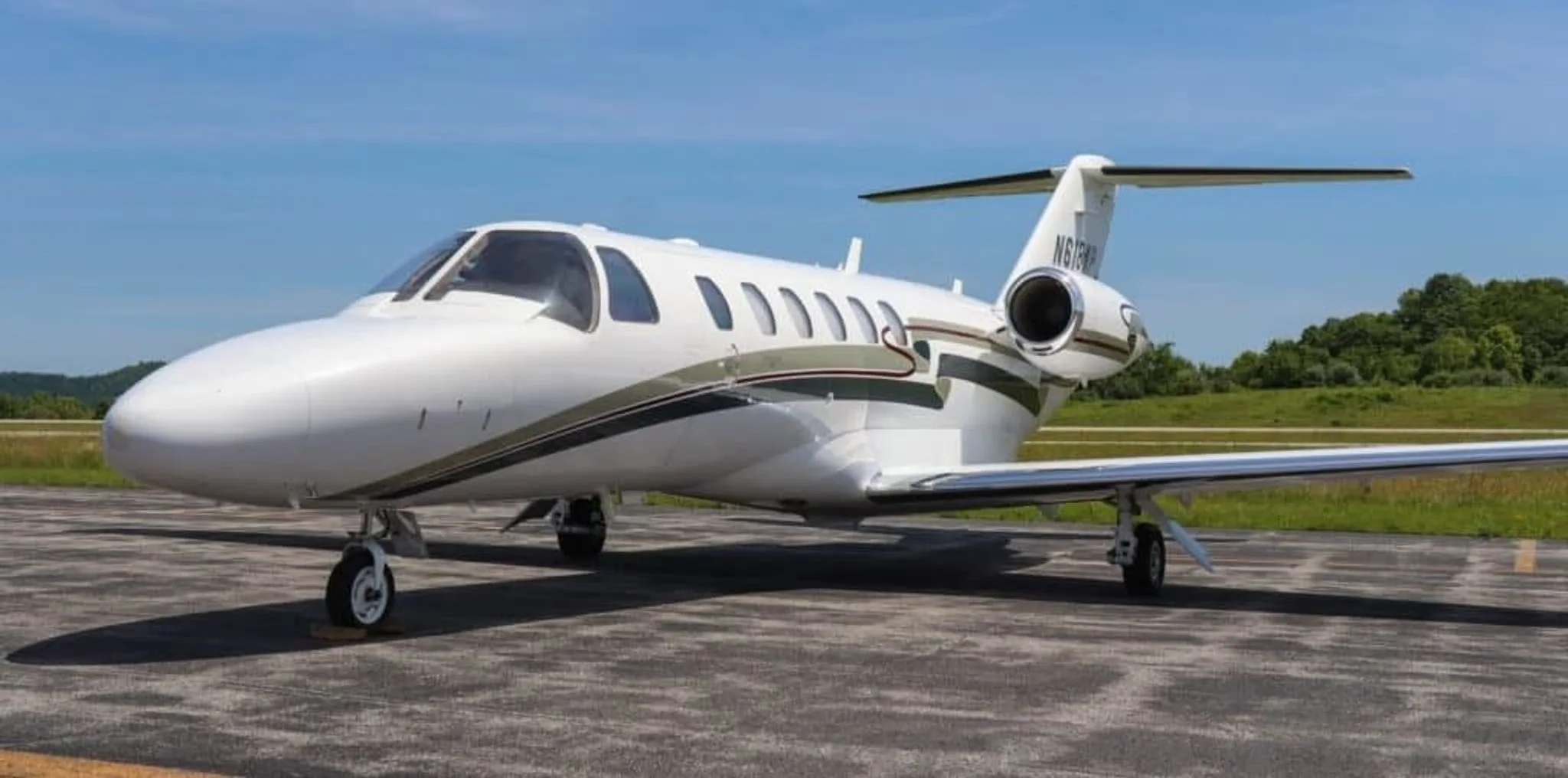 A low-angle front-quarter view of a white Cessna Citation CJ2+ business jet with green and red stripes on an airfield.