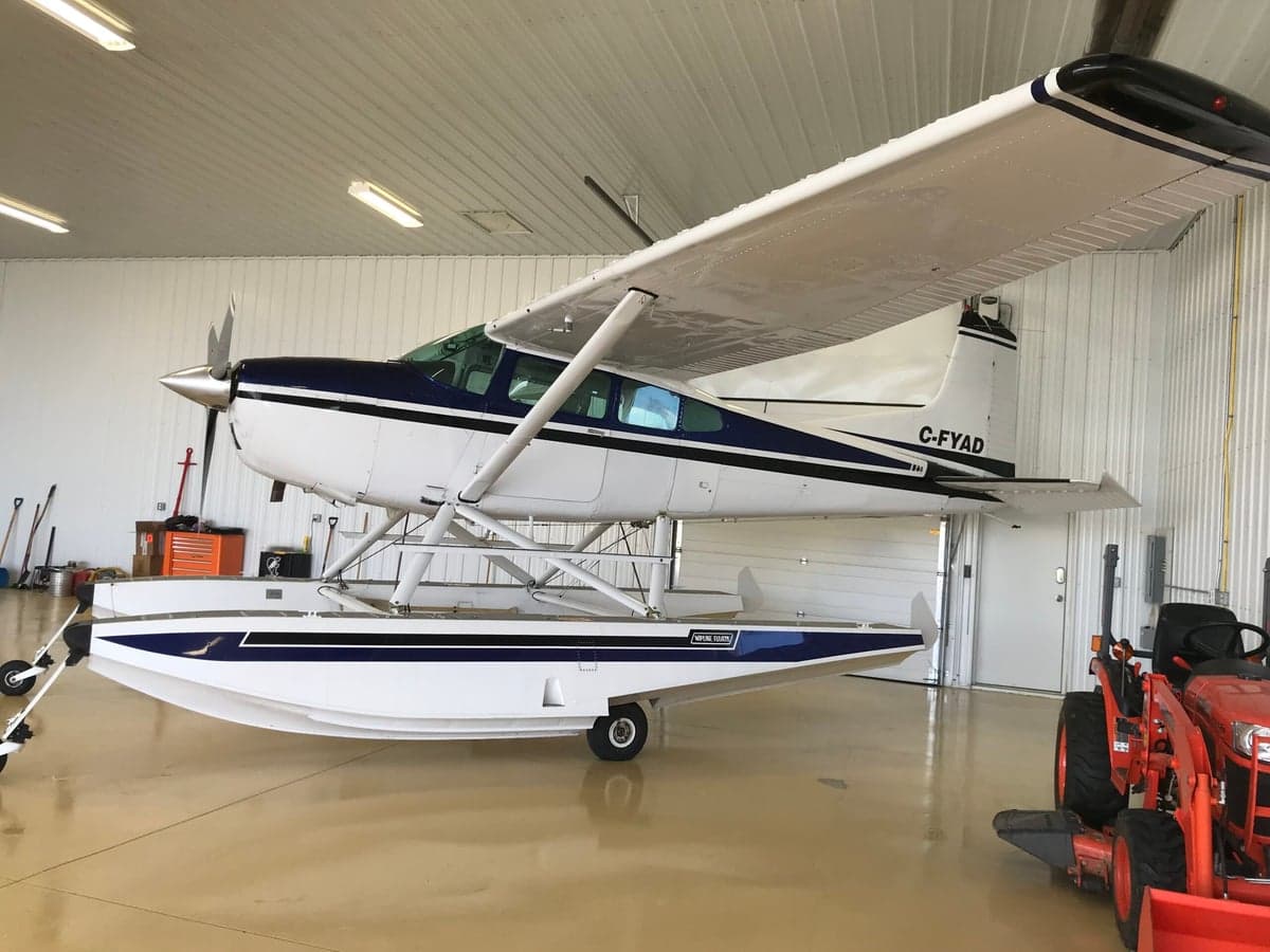 Side view of a white and blue Cessna on floats inside a hangar.