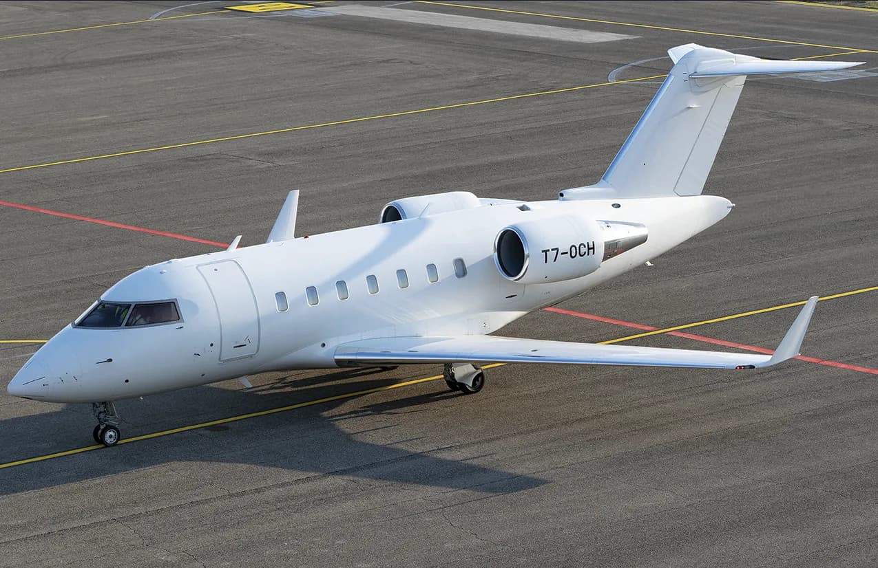 An all-white Bombardier Challenger business jet with registration T7-0CH is parked on an airport tarmac.