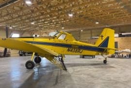 Side view of a yellow and blue agricultural aircraft with the tail number N438RJ in a hangar.
