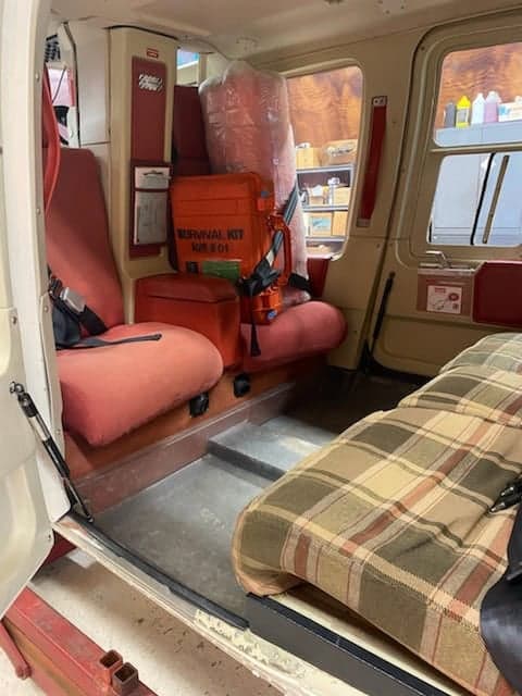 The interior of a Bell 206L-4 LongRanger helicopter with red seats and a survival kit.