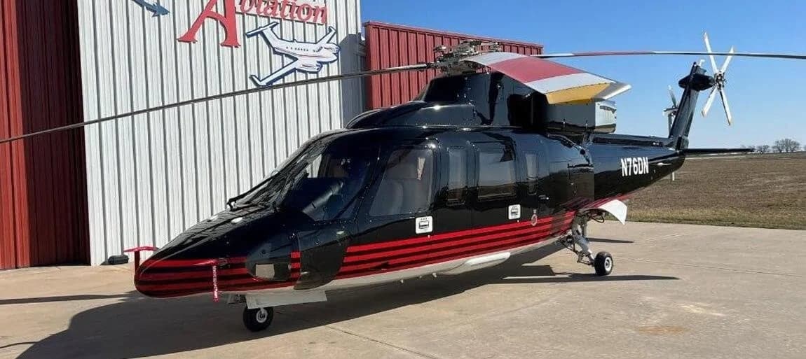 A black and red Bell 222 helicopter parked outside a hangar.