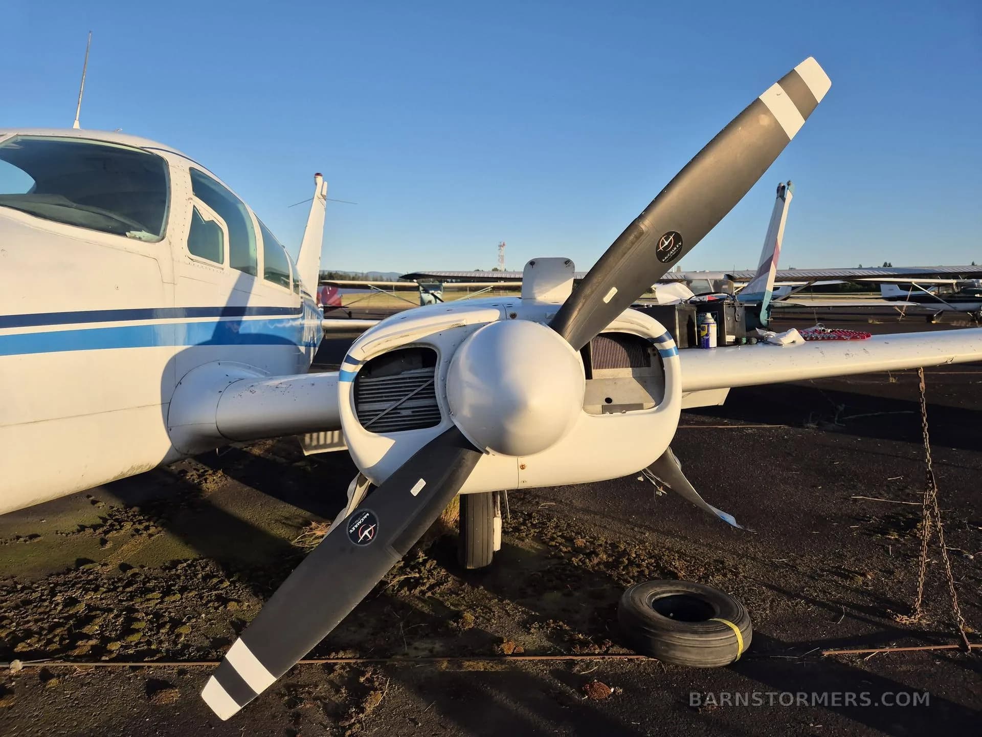 A close-up view of the right engine and propeller of a white twin-engine aircraft with blue stripes, showing the engine cowling partially open.