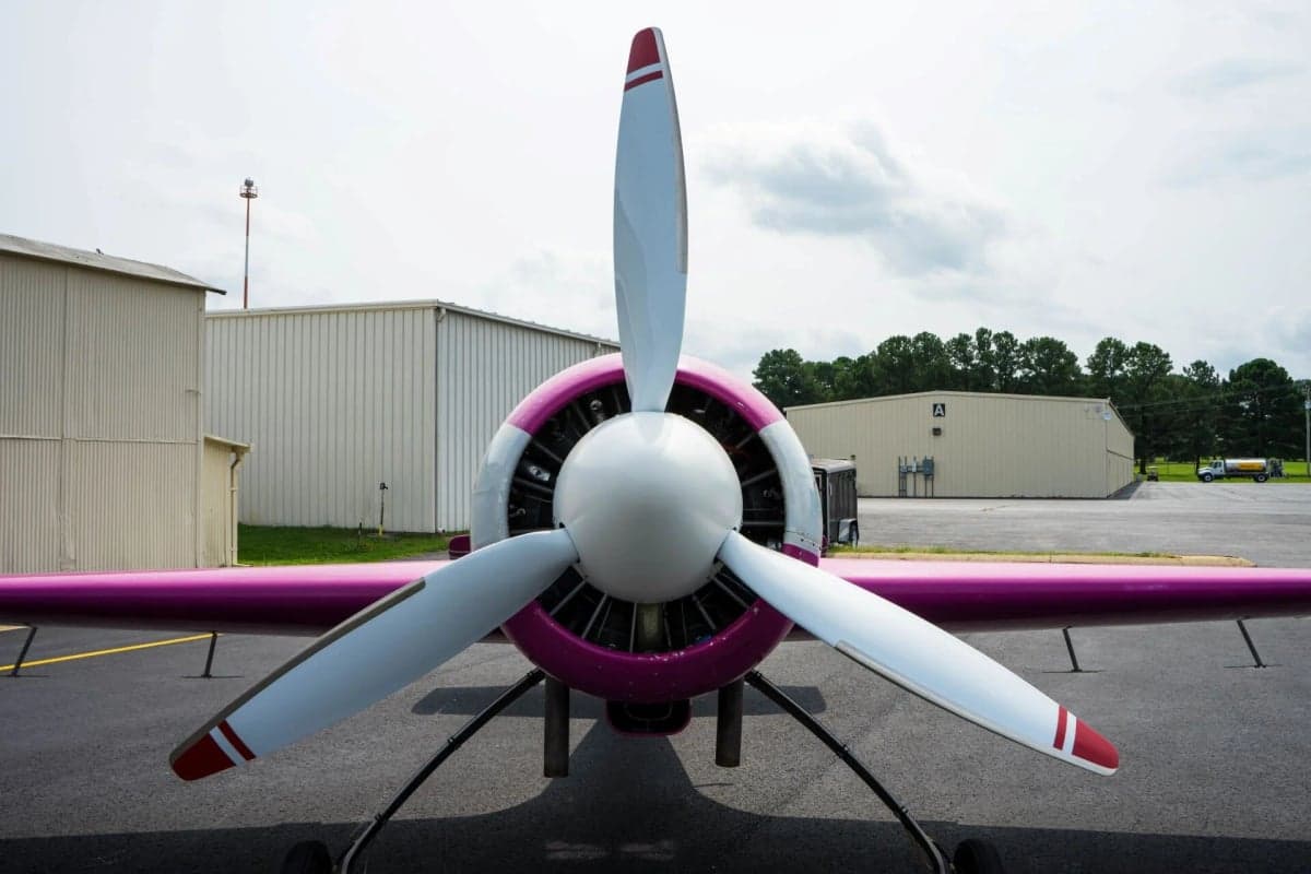 Front view of a pink and white Sukhoi Su-26 aircraft with a three-blade propeller.