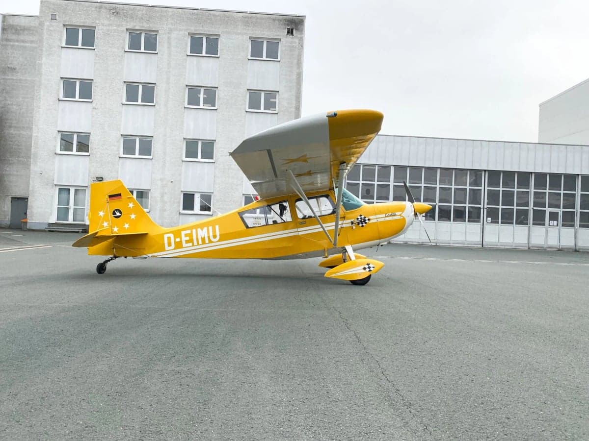 Front view of a yellow and white aircraft, D-EIMU, parked on the tarmac in front of a hangar.