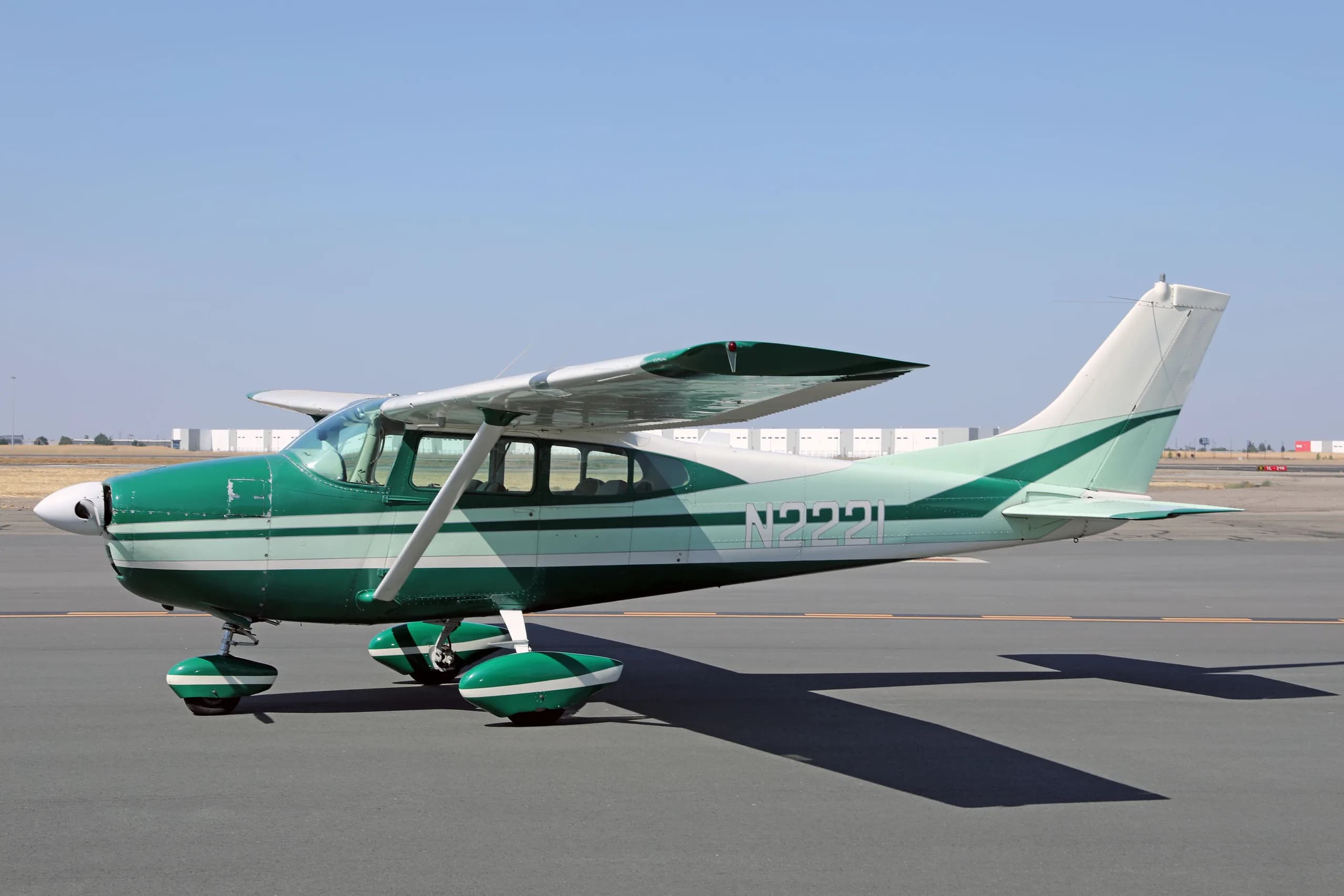 A green and white Cessna 182 Skylane N2221 parked on an airfield tarmac under a clear sky.