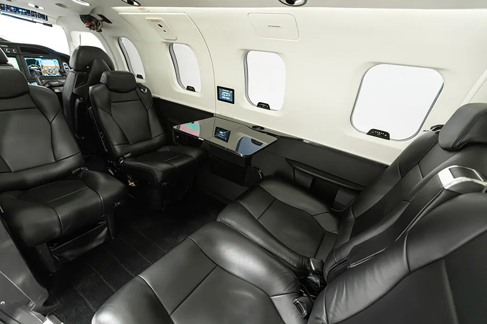 View of a private jet cabin with black leather seats and a side table.