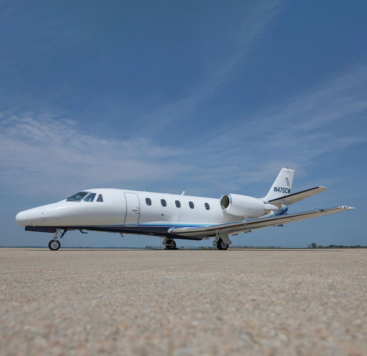 Side view of a white jet with blue accents on the tarmac.