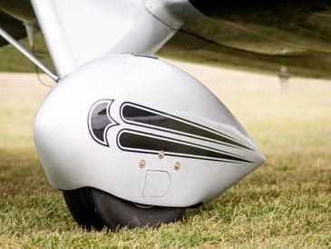 A man stands on the wing of a silver biplane on a grassy field.