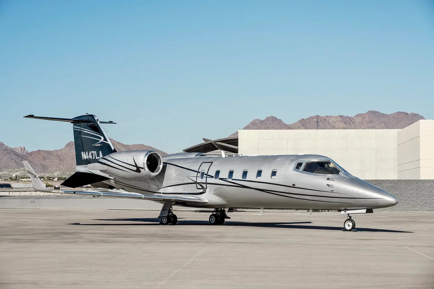 Learjet 45XR, registration N447LA, parked on the tarmac with mountains in the background.