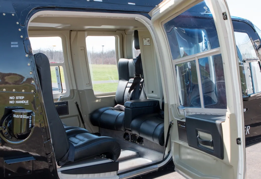 The black leather passenger seats in the helicopter's cabin, viewed from the right side with the door open.