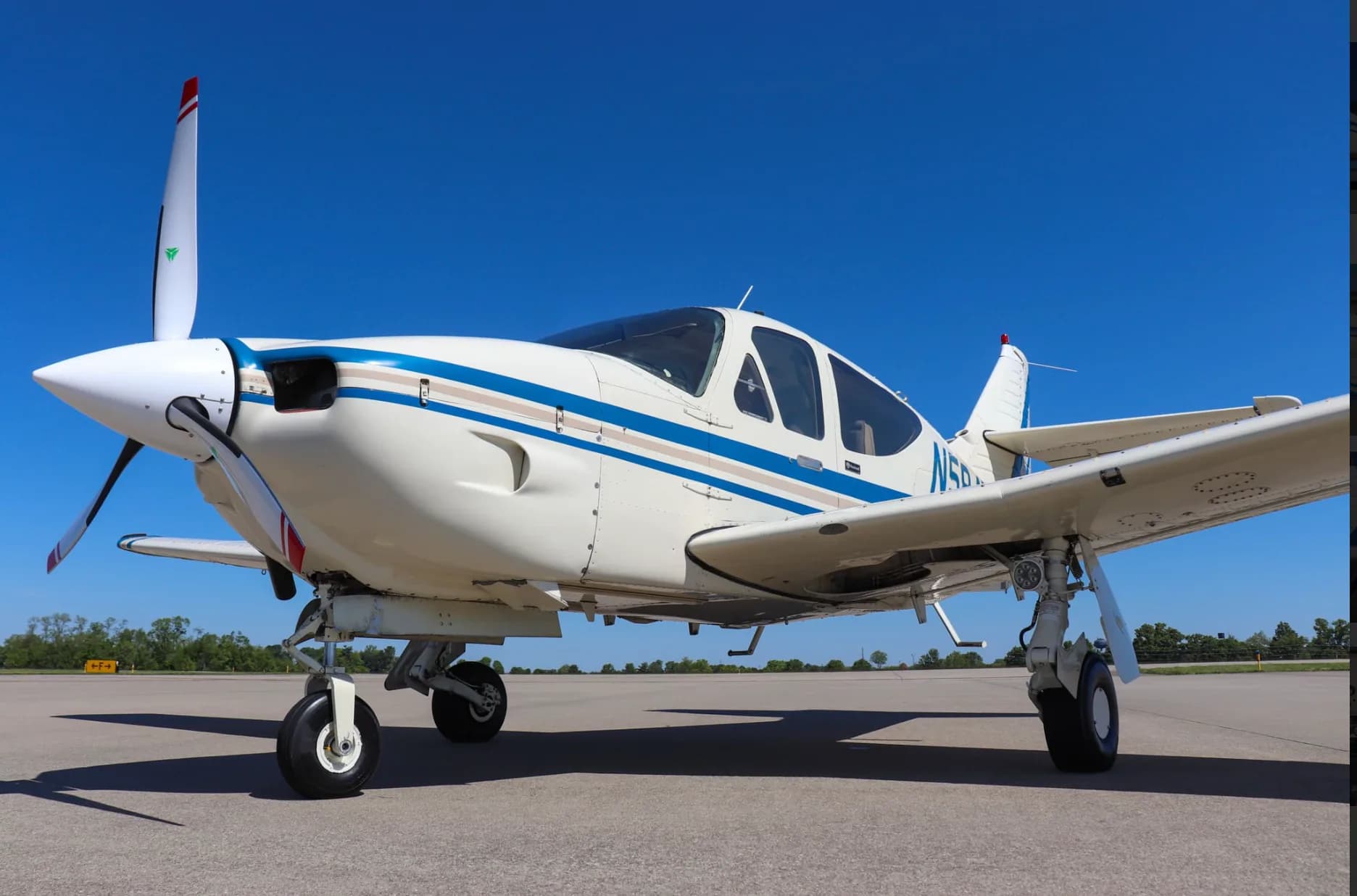 Low-angle side view of a white single-engine propeller aircraft with blue and tan stripes, registration N5842N, parked on an airfield.