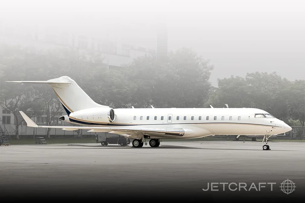 A full side view of a white business jet with a gold and blue stripe, parked on a foggy airfield.