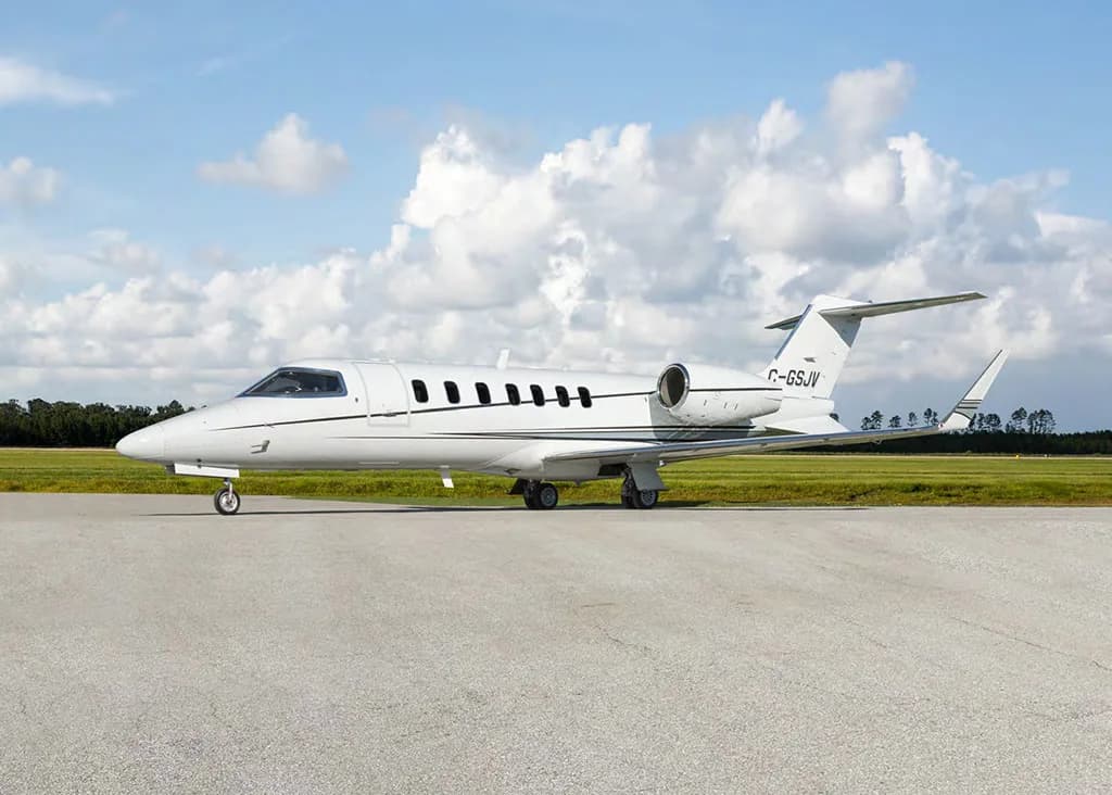 A white Learjet 75 business jet with a black stripe, registration C-GSJV, parked on a tarmac under a partly cloudy sky.