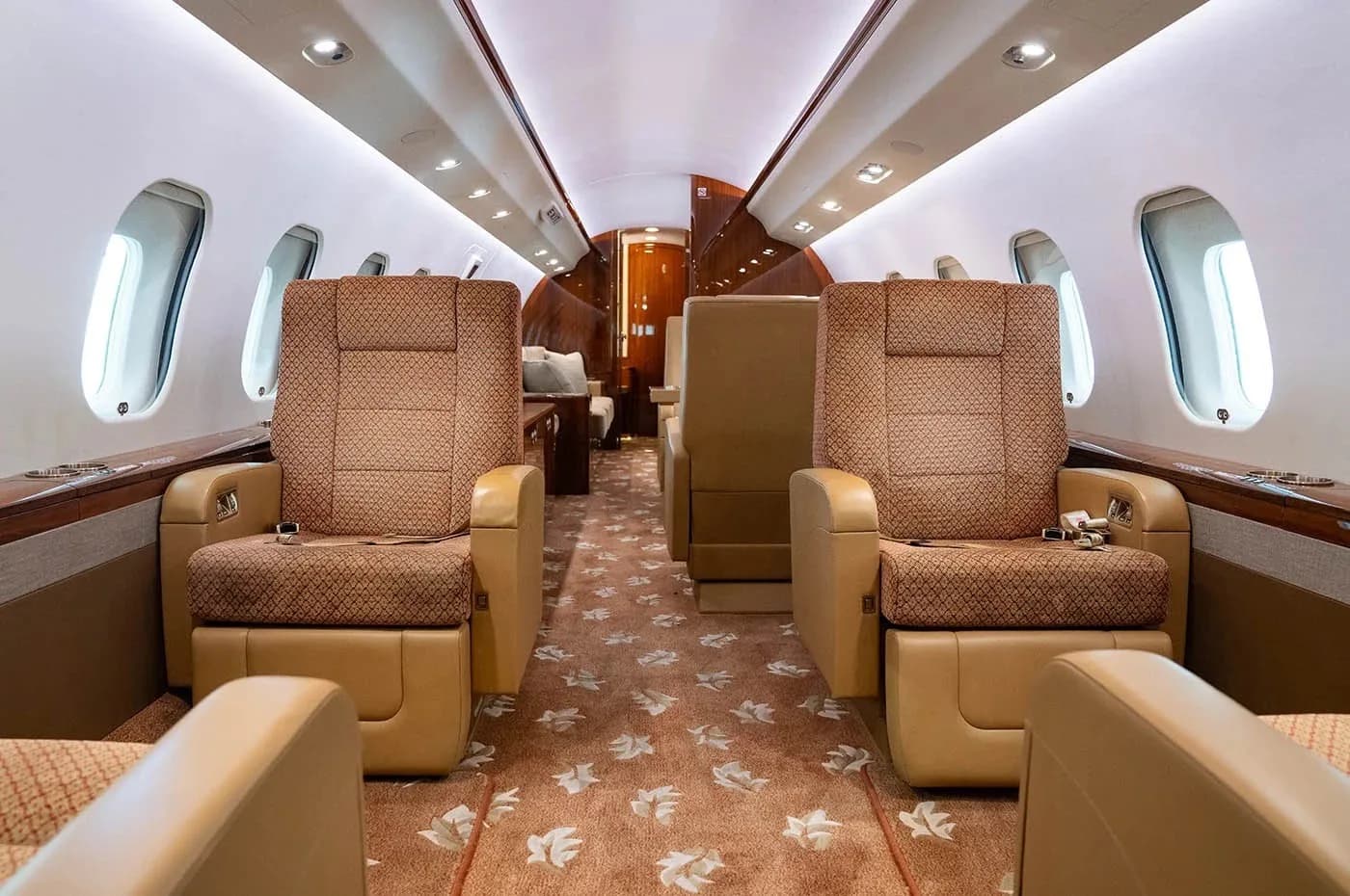 A view down the aircraft cabin aisle shows multiple individual seats with patterned upholstery and a patterned carpet.