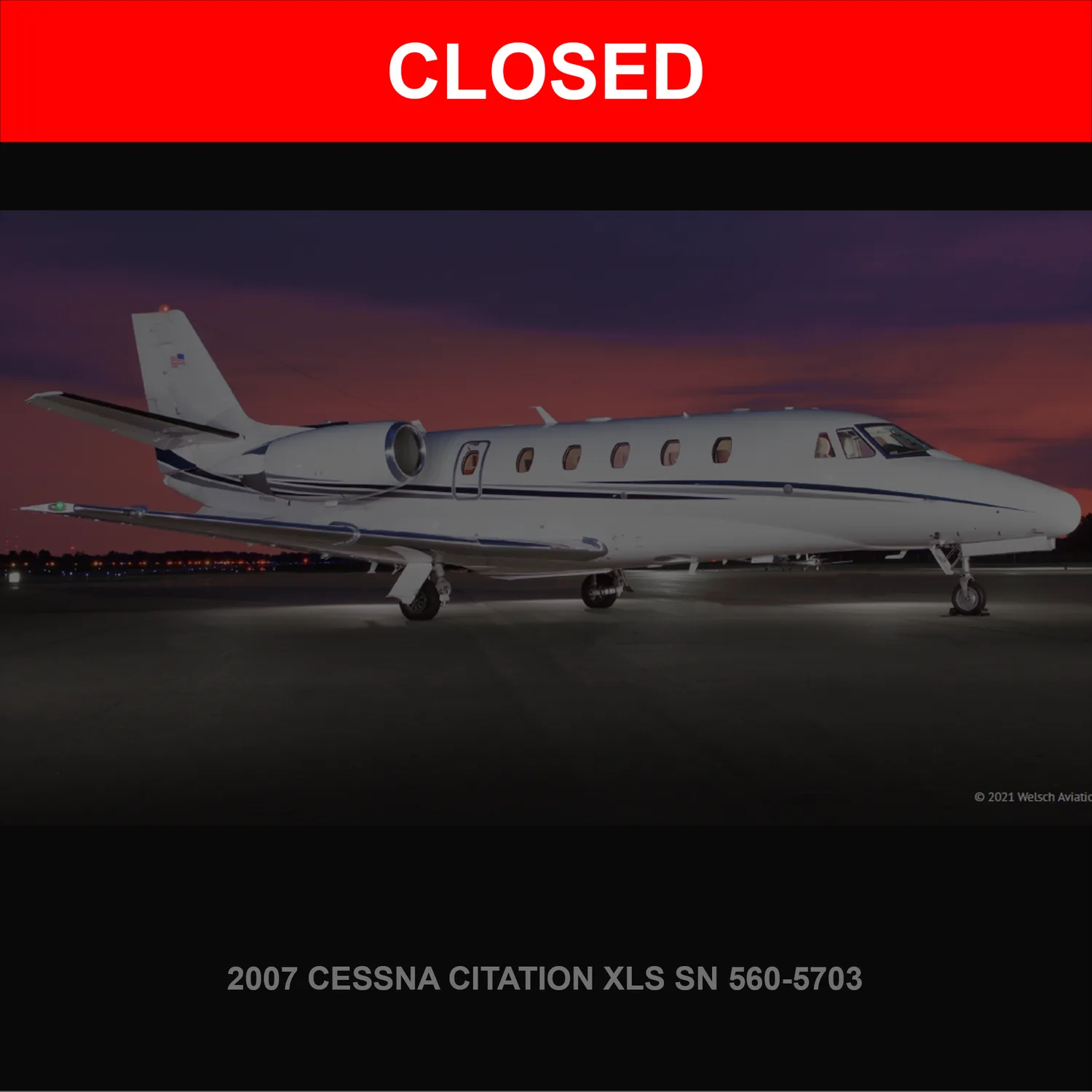 A white Cessna Citation XLS business jet with blue stripes is parked on a tarmac at dusk.