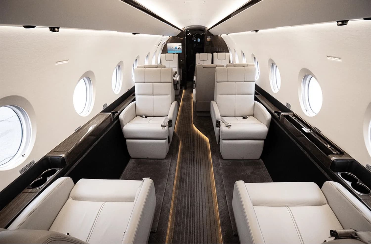 The spacious interior cabin of a private jet with light-colored leather seats, large windows, and overhead lighting.