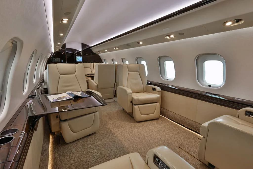 A view inside the business jet cabin, showing beige leather seating arrangements and a polished table.