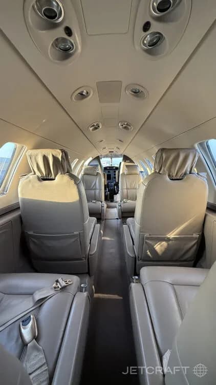The interior cabin of a private jet with light brown leather seats, looking forward towards the cockpit.