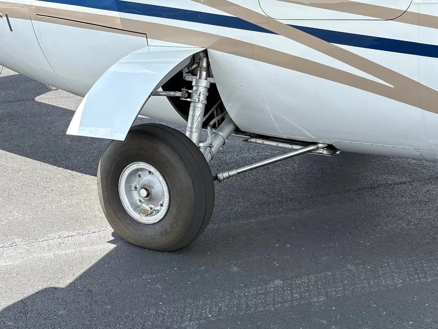 Close-up of the main landing gear and wheel of a white aircraft with blue and gold stripes.