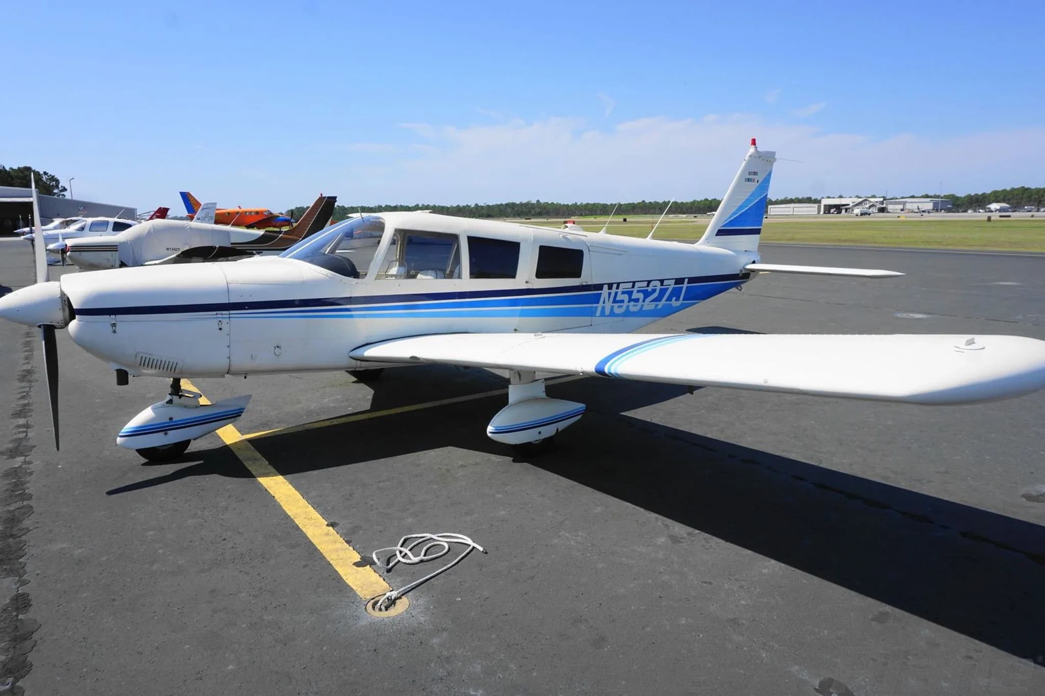 Side view of the white N5527J single-engine propeller aircraft with blue stripes on an airport tarmac.