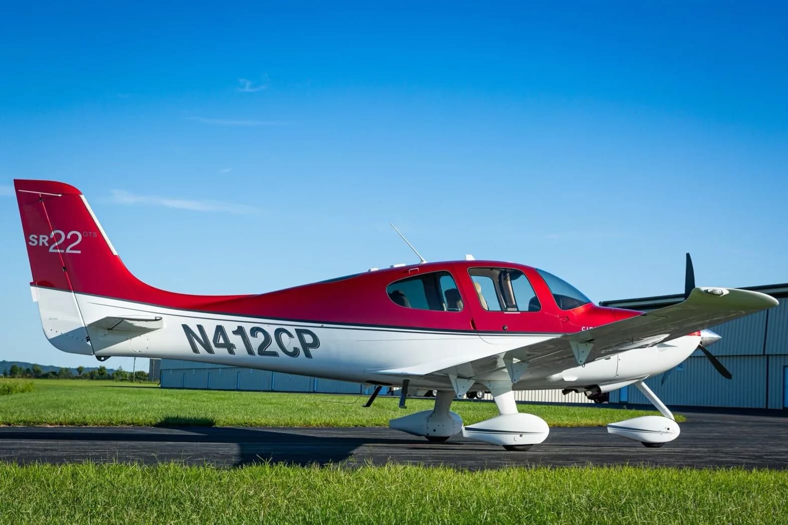 A red and white Cirrus SR22 GTS aircraft (N412CP) parked on an airfield next to a hangar.