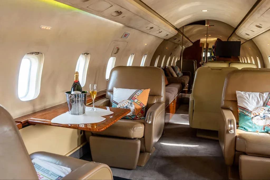 A private jet cabin interior with tan leather seats, a table with champagne, and a view towards the rear.