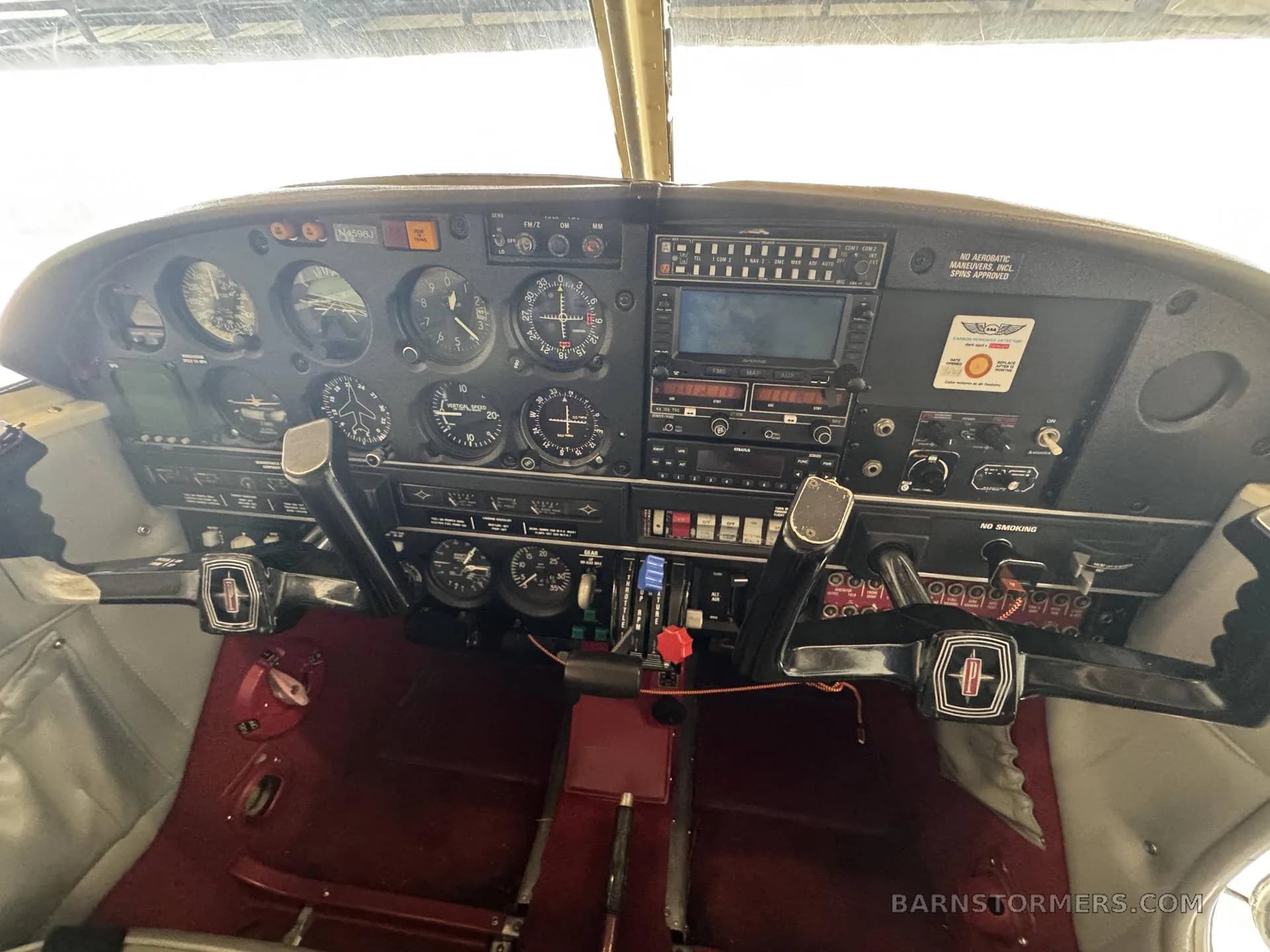 The cockpit of a Piper Cherokee Arrow, showing the instrument panel, yokes, and red carpet.