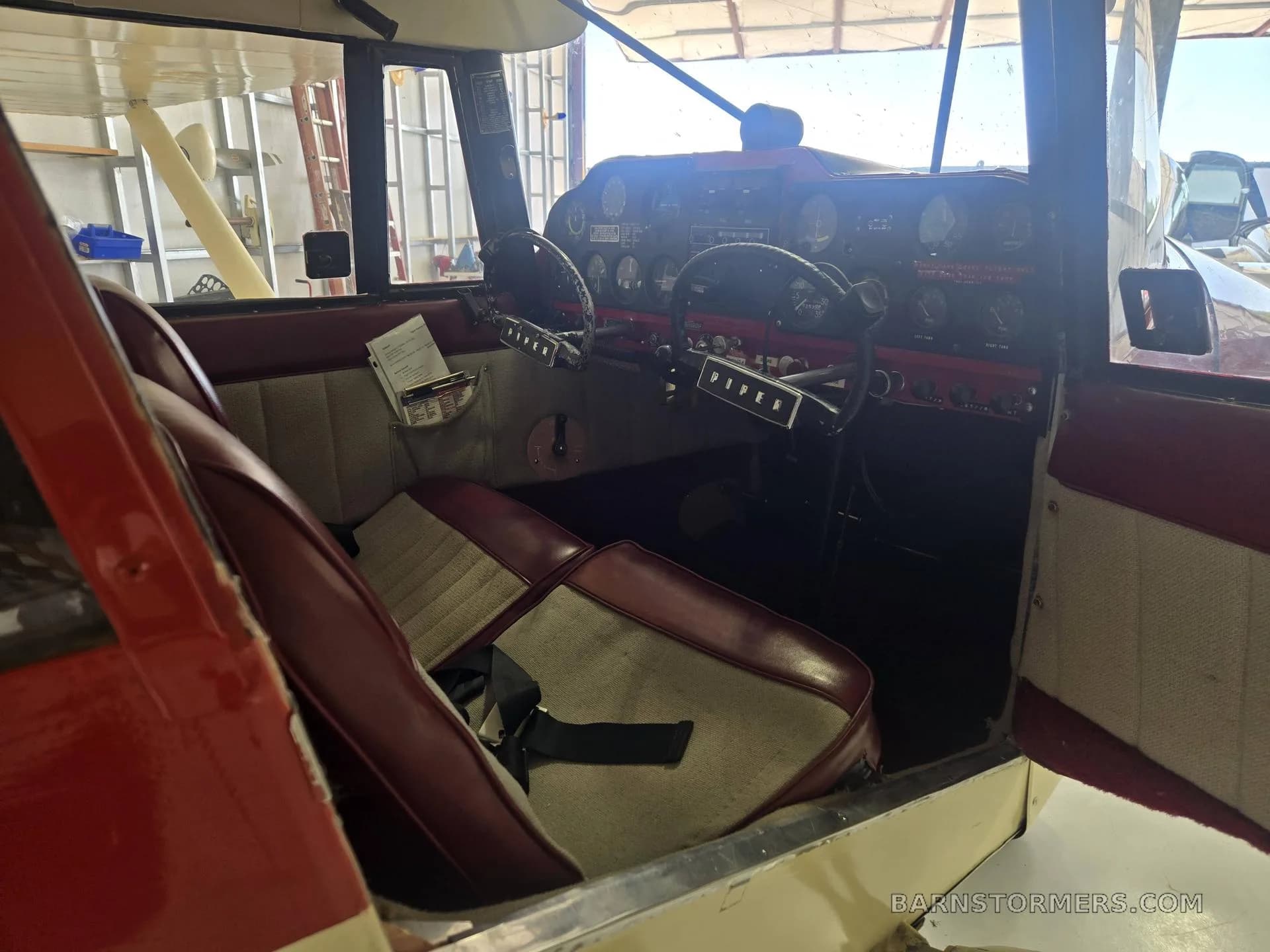 The interior of a small aircraft, showing red and beige seats and the instrument panel from a side view.