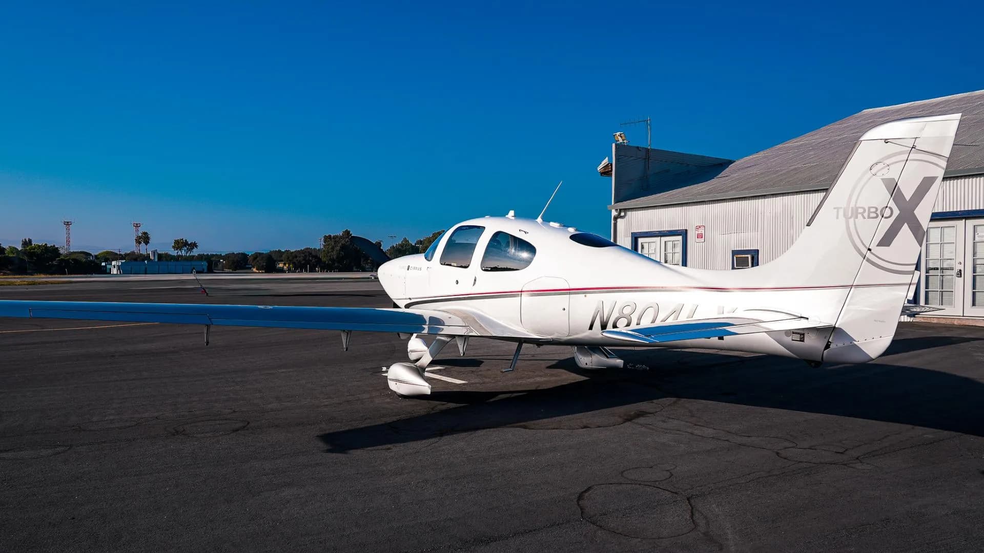 A three-quarter rear view of the white and silver Cirrus SR22T aircraft N804LX with a clear blue sky.