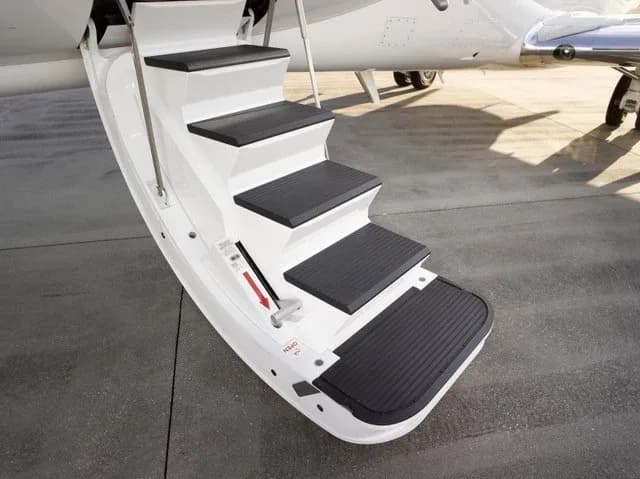 A close-up view of the white retractable airstairs of a business jet with black non-slip treads.