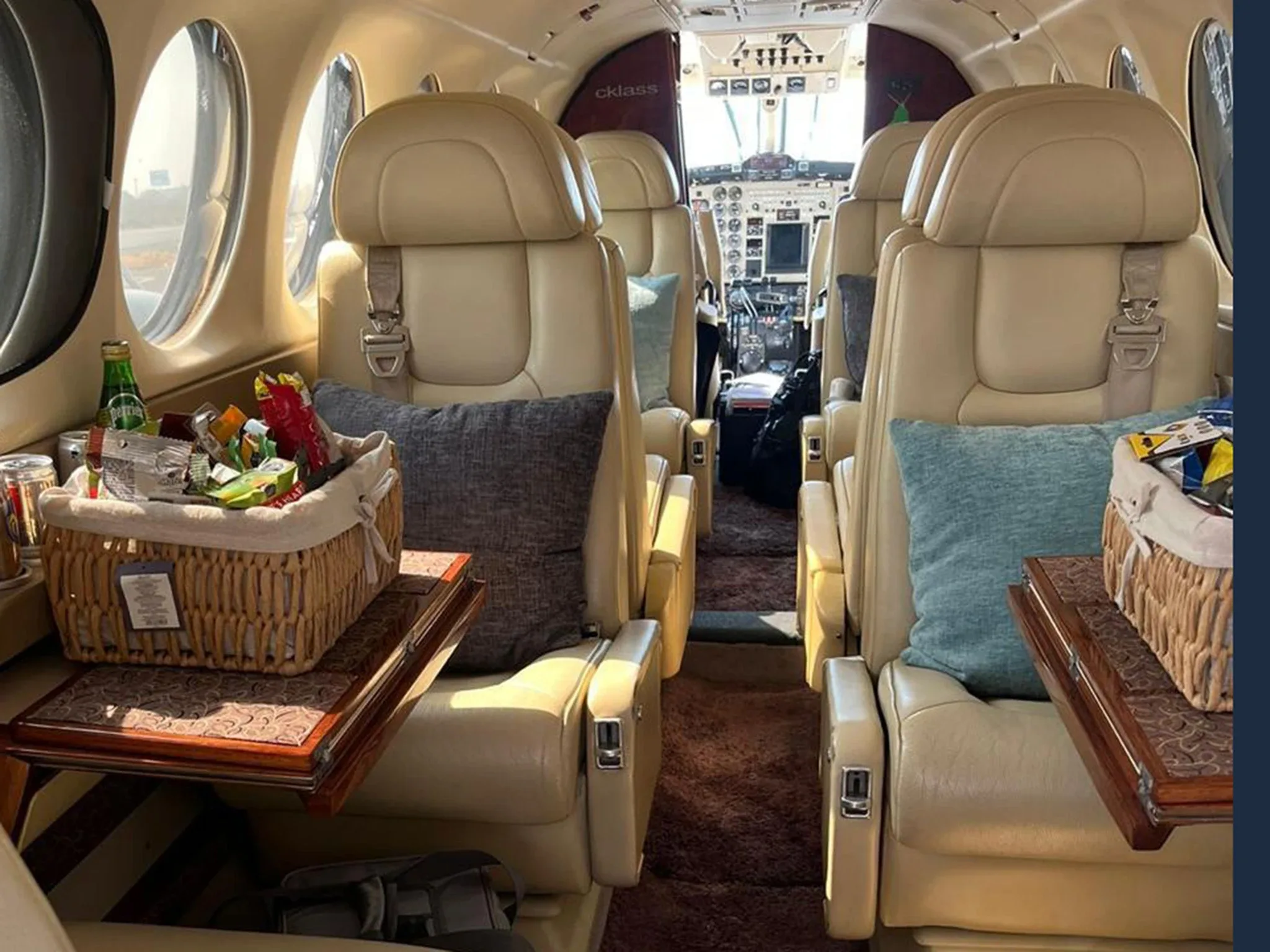 The aircraft cabin interior showing beige leather seats, pillows, and a basket of snacks on a table.