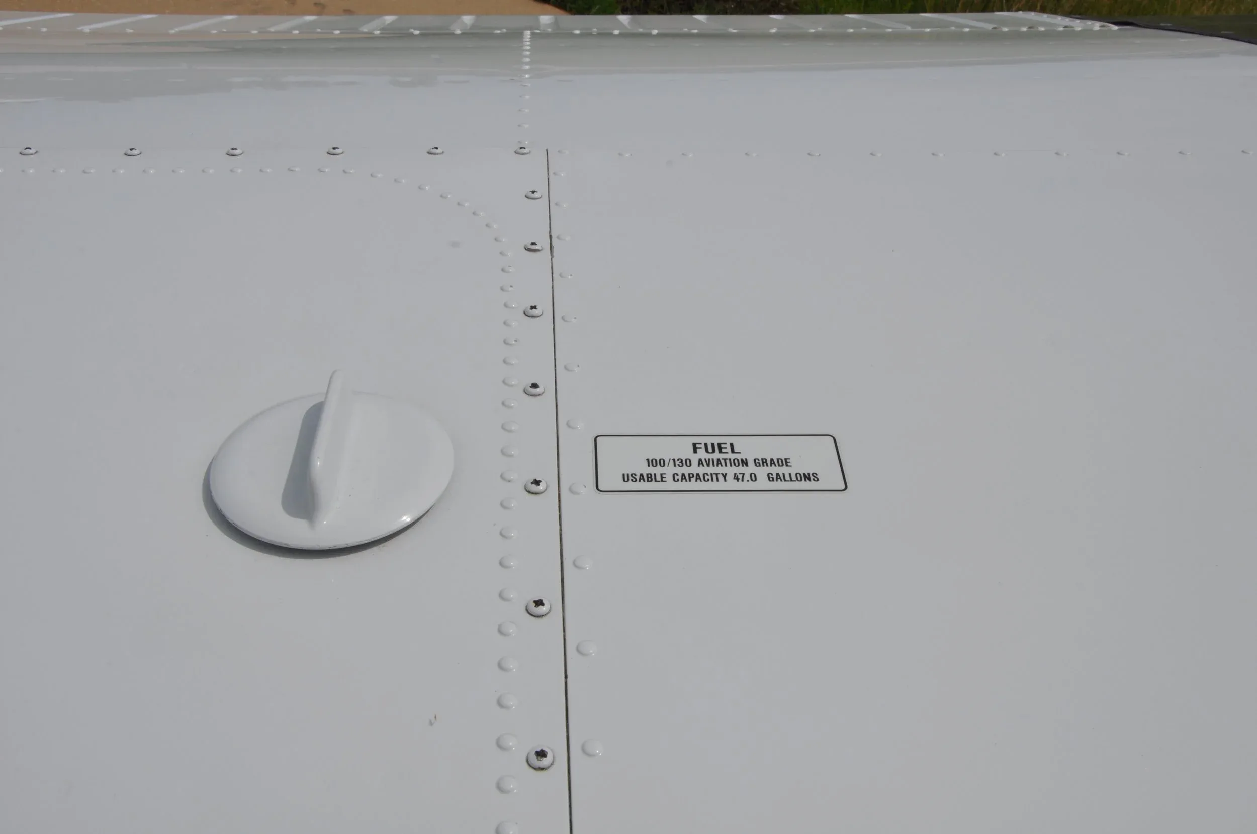 A close-up of a fuel cap and label on the aircraft wing, indicating fuel type and capacity.