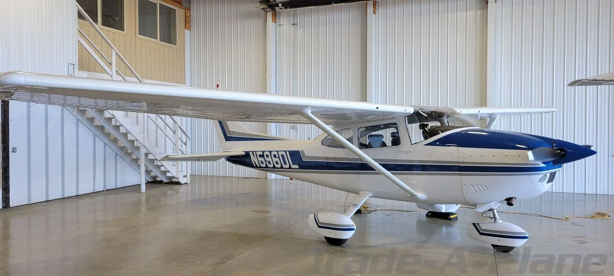 A white and blue Cessna 182 Skylane aircraft parked inside a hangar.