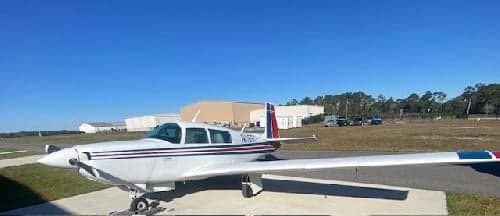 A Beechcraft Bonanza with a white and blue paint scheme is parked on the tarmac.