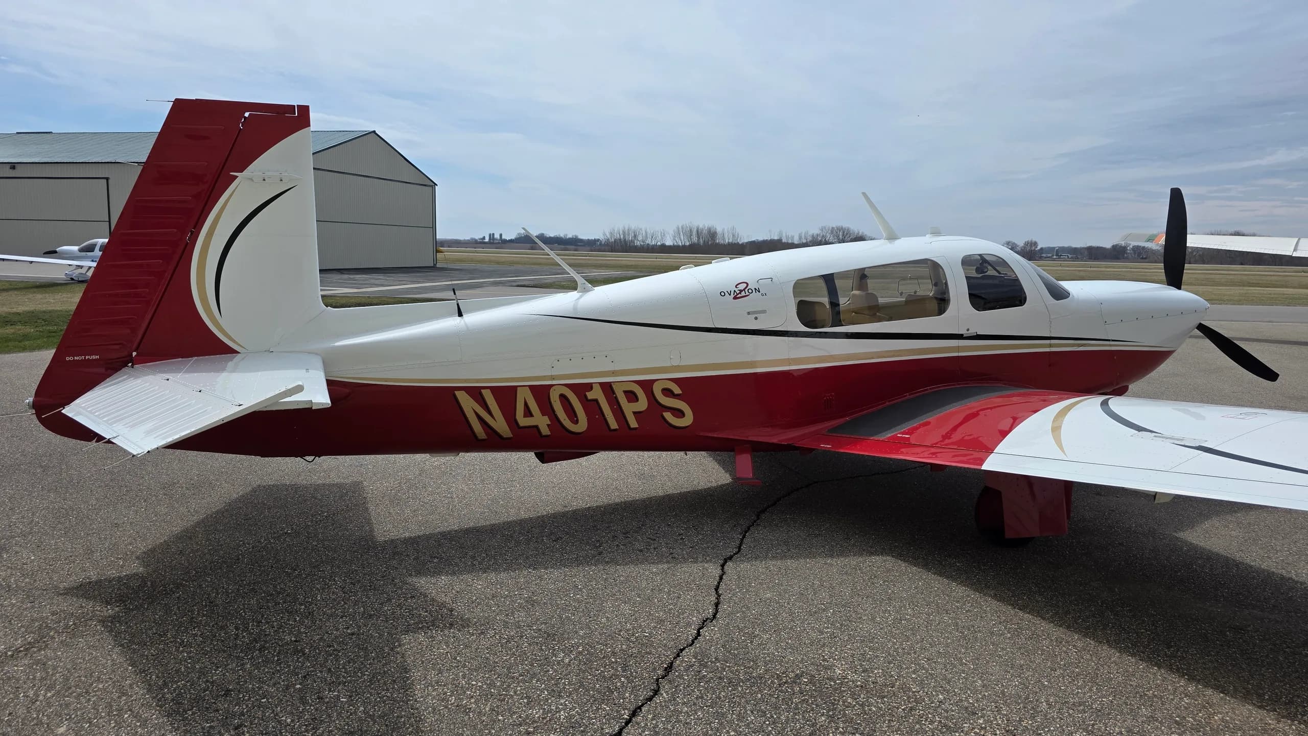 A red and white Mooney aircraft with registration N401PS parked on an asphalt apron, viewed from the rear right.