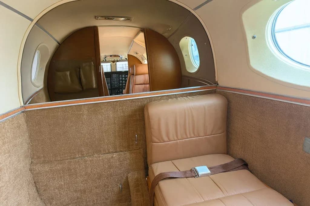 A view from the rear of the aircraft cabin, showing a tan seat and the curved bulkhead leading to the main seating area.